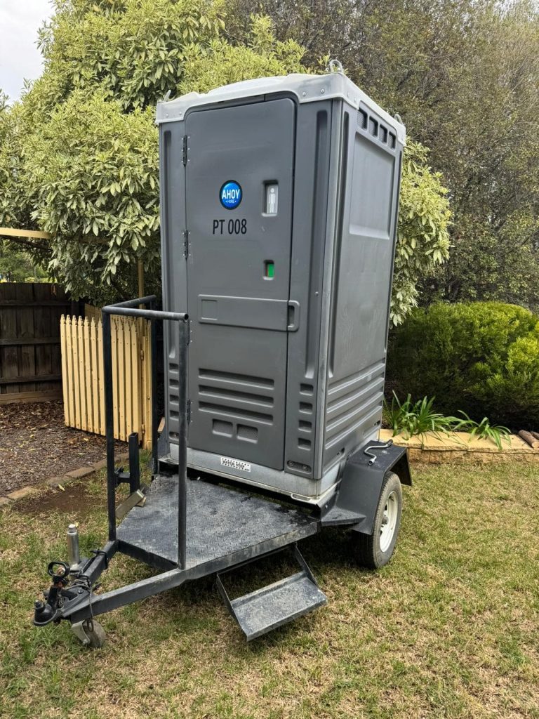 Ahoy Hire portable toilet on trailer parked on lawn.