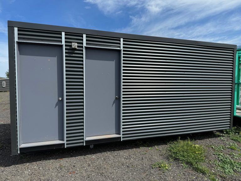 Grey corrugated metal site shed with dual doors on gravel lot.