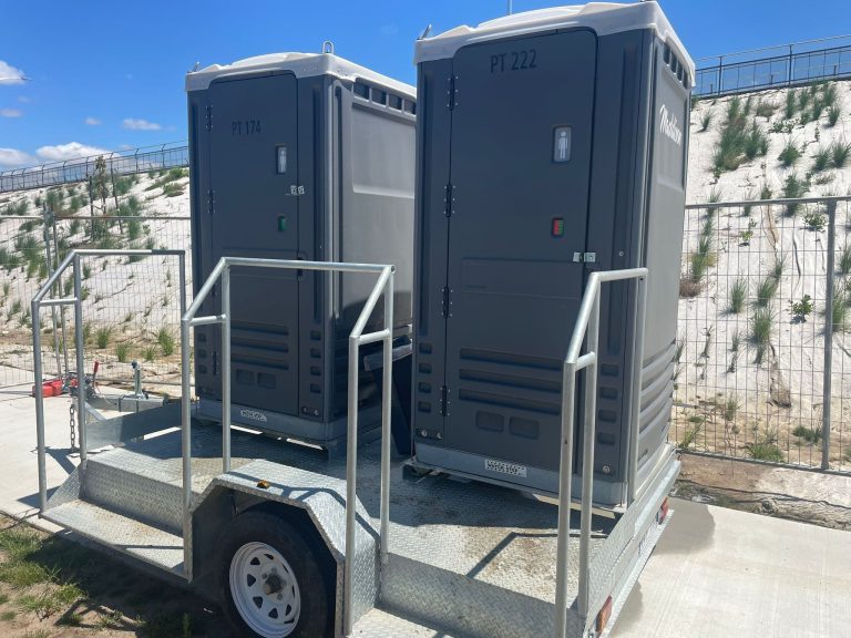 Two portable toilets on trailer at construction site.