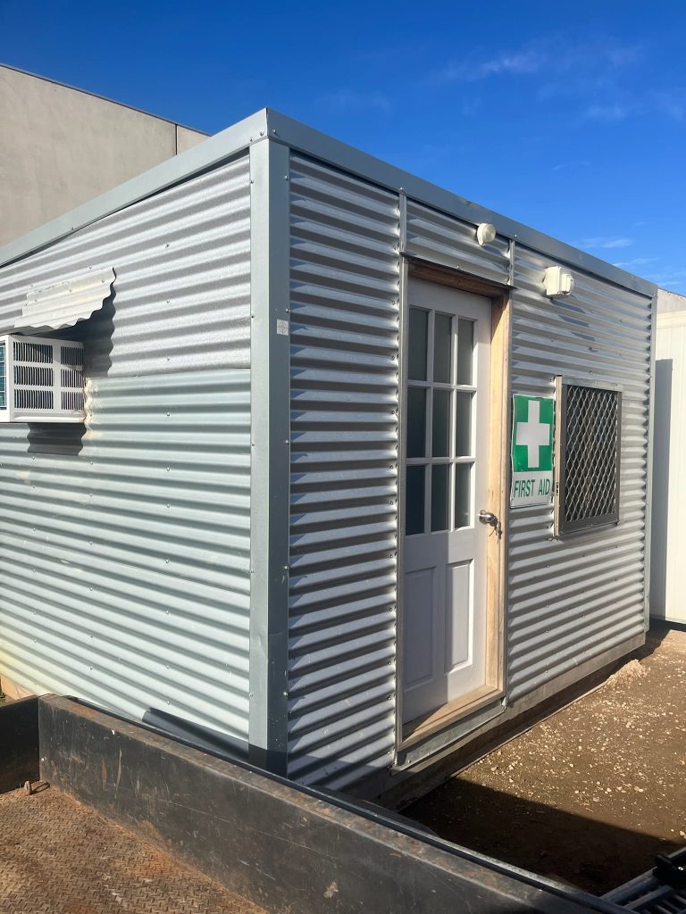 Corrugated metal site shed with first aid signage.