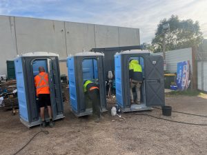 Workers cleaning portable toilets at construction site.
