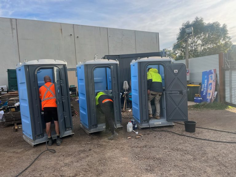 Workers cleaning portable toilets at construction site.