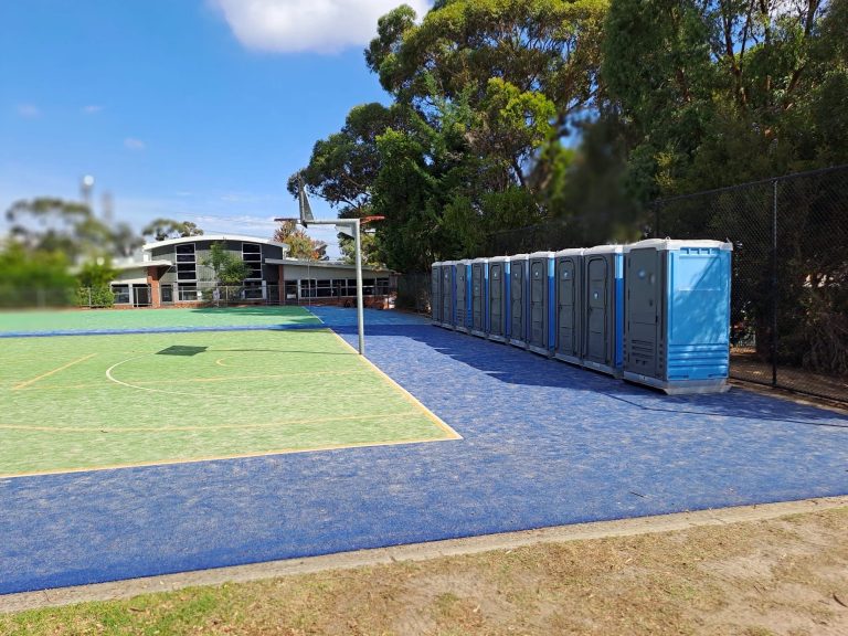 Row of portable toilets placed on outdoor sports court.