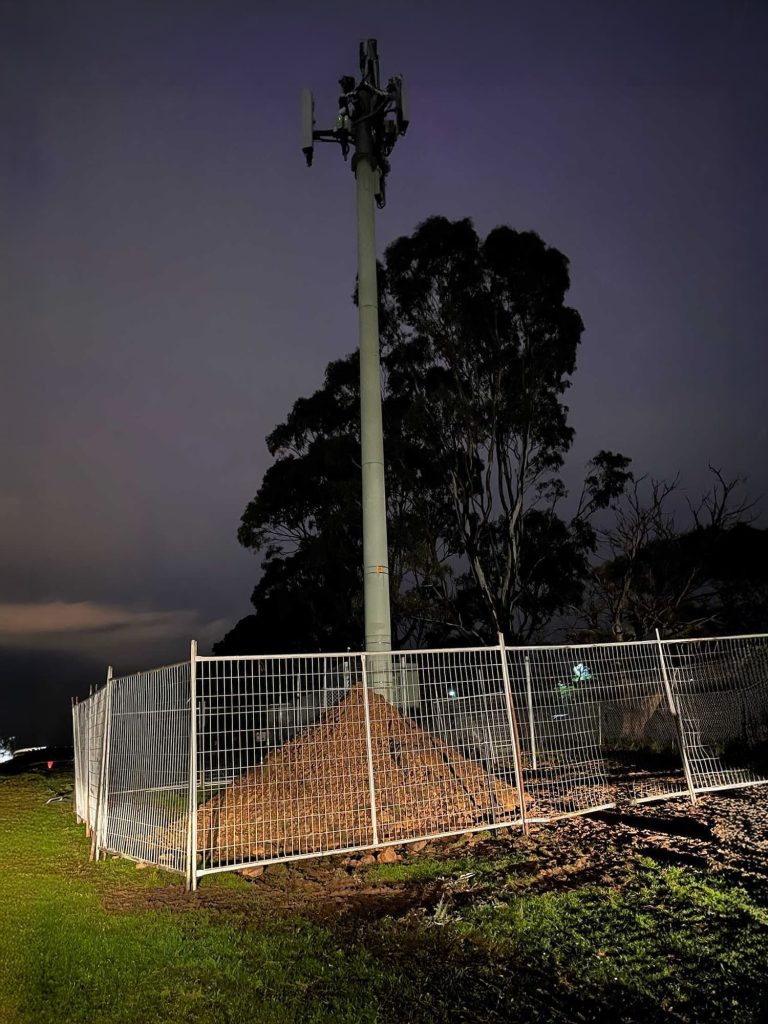 Temporary fencing around Vodafone tower at night.